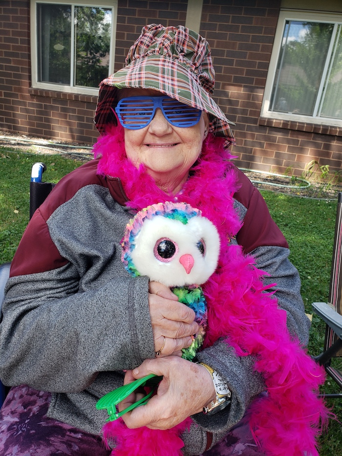 Breath of Life Participant on fun dress up theme day wearing. a pink boa outside holding an owl and wearing a hat and glasses!
